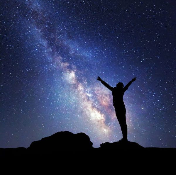 Milky Way. Night sky with stars and silhouette of a woman with raised-up arms.